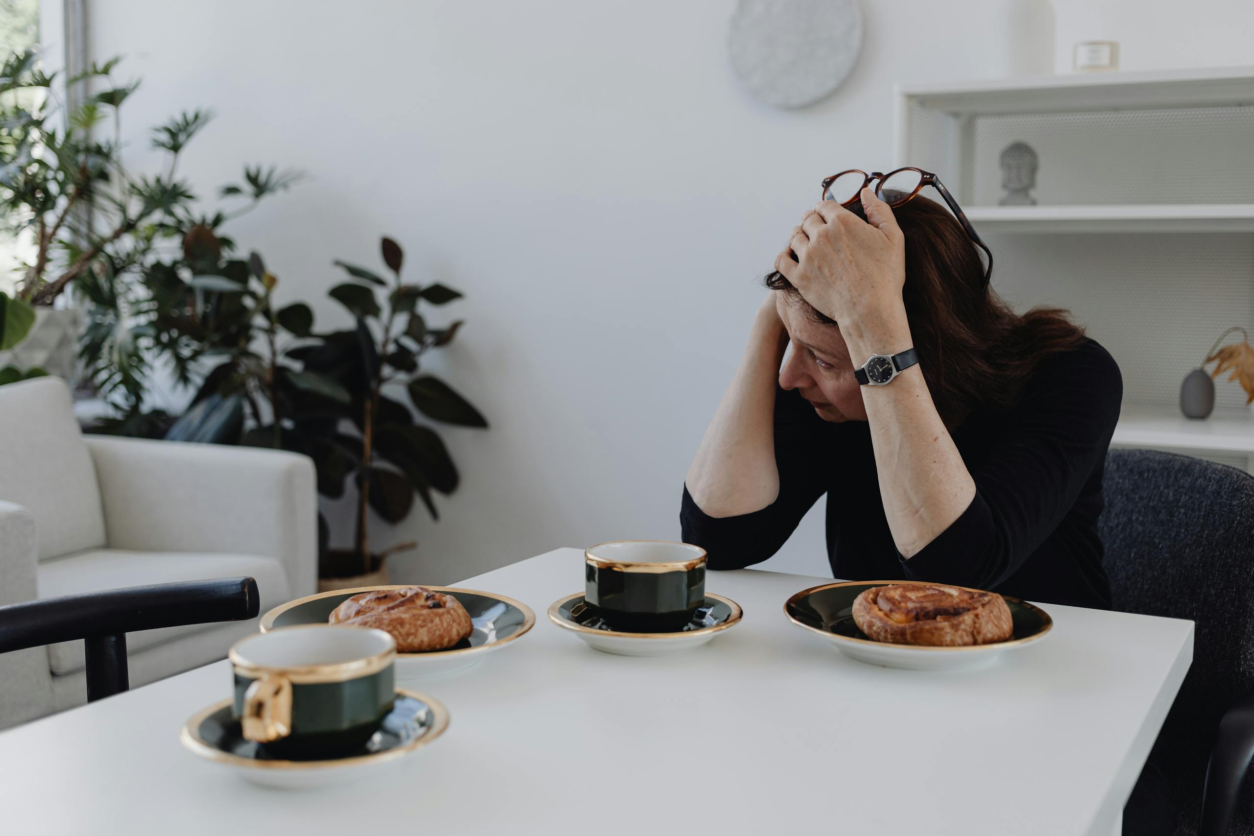 A woman sits at a table with coffee and pastries, embodying solitude and introspection indoors.