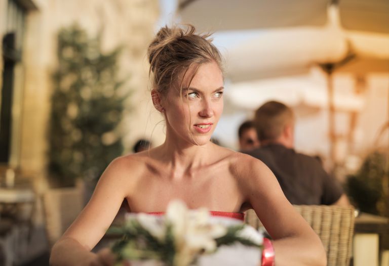 A woman sits in an outdoor cafe, enjoying a sunny day. She appears relaxed and thoughtful, embodying a sense of leisure.