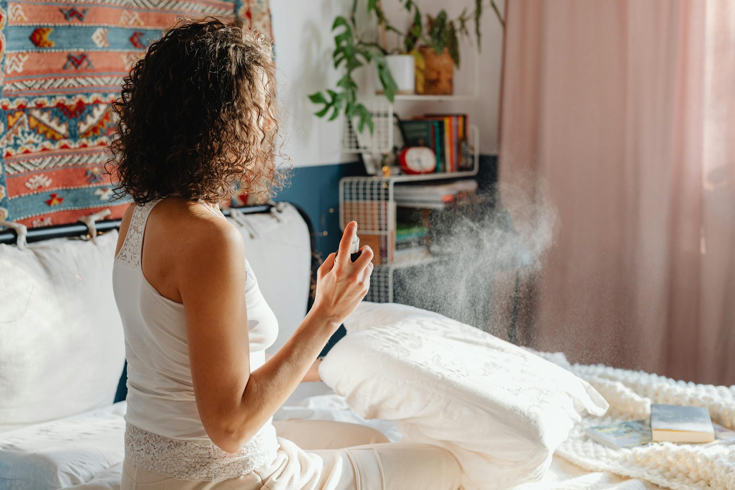 A woman sits on her bed, spraying a fragrant mist to refresh the room.