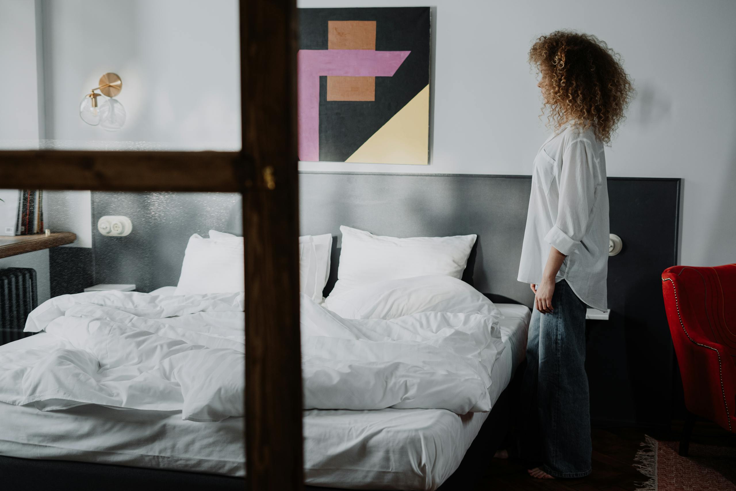 A woman standing in a cozy bedroom with modern art, showcasing a comfortable and stylish interior.