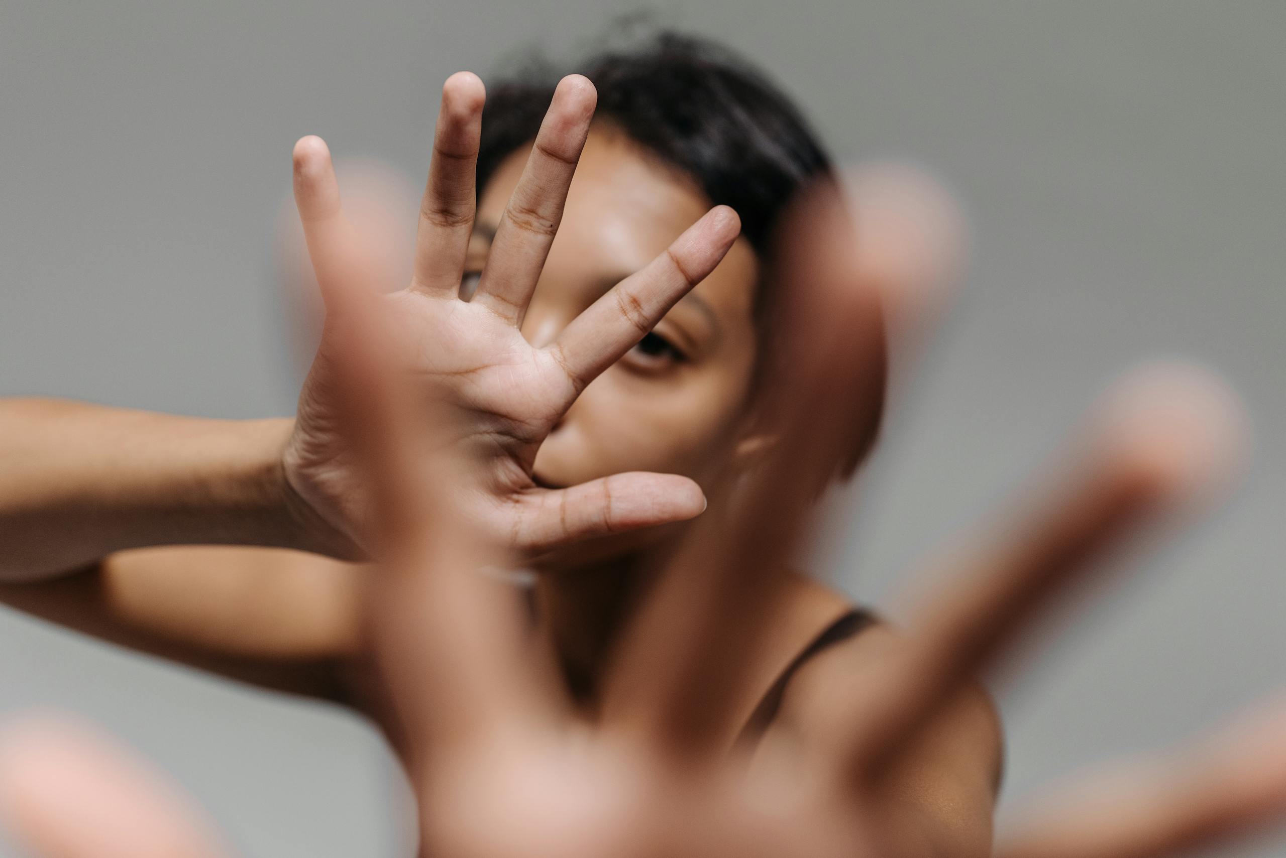 A woman uses hands to obscure her face against a gray backdrop.