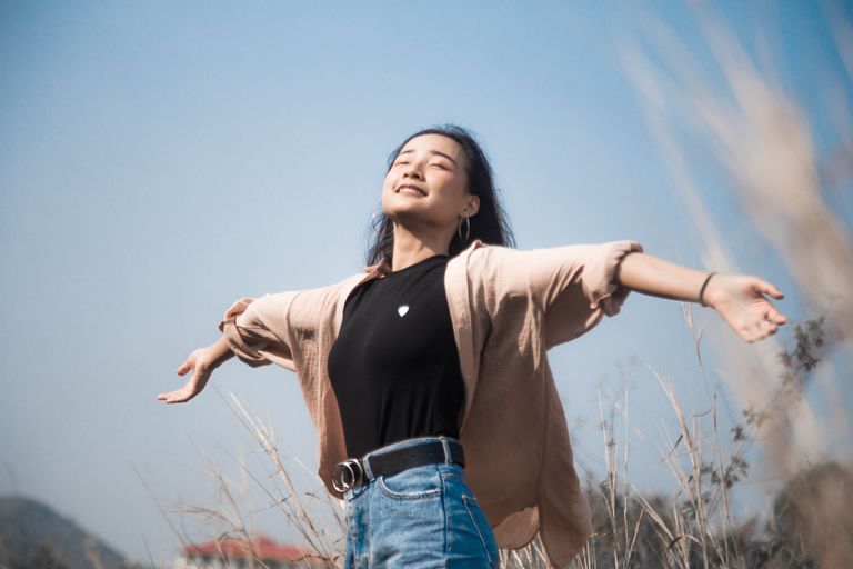 A woman with arms outstretched enjoys a sunny day in a natural field setting.