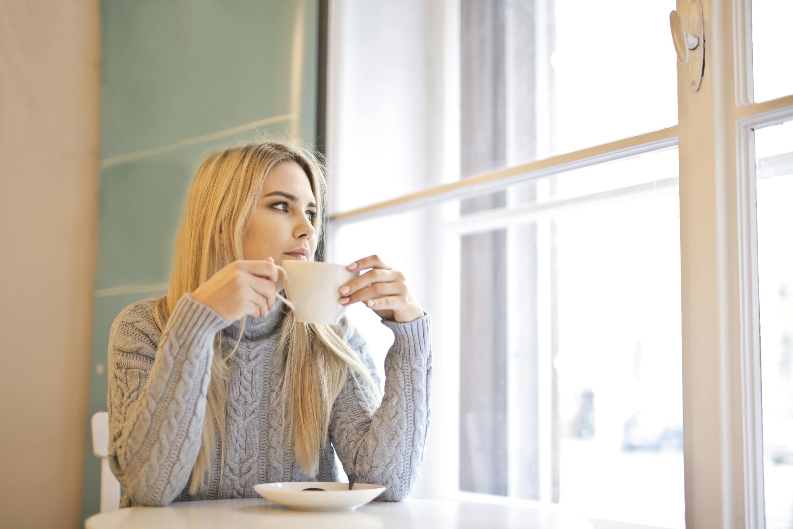 A woman with blonde hair enjoys a warm coffee in a cozy indoor cafe setting.