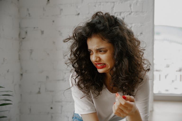 A woman with curly hair and red lips expresses a disgusted facial expression indoors.