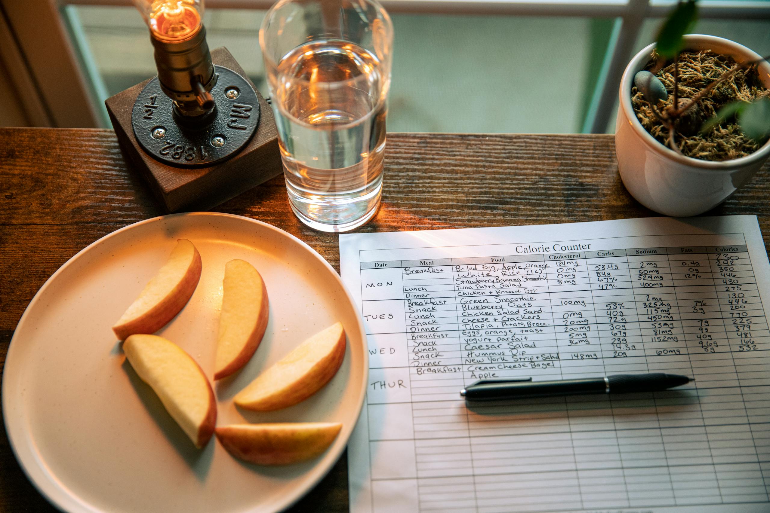 A wooden table setup with apple slices, a calorie chart, and a glass of water for a healthy diet plan.