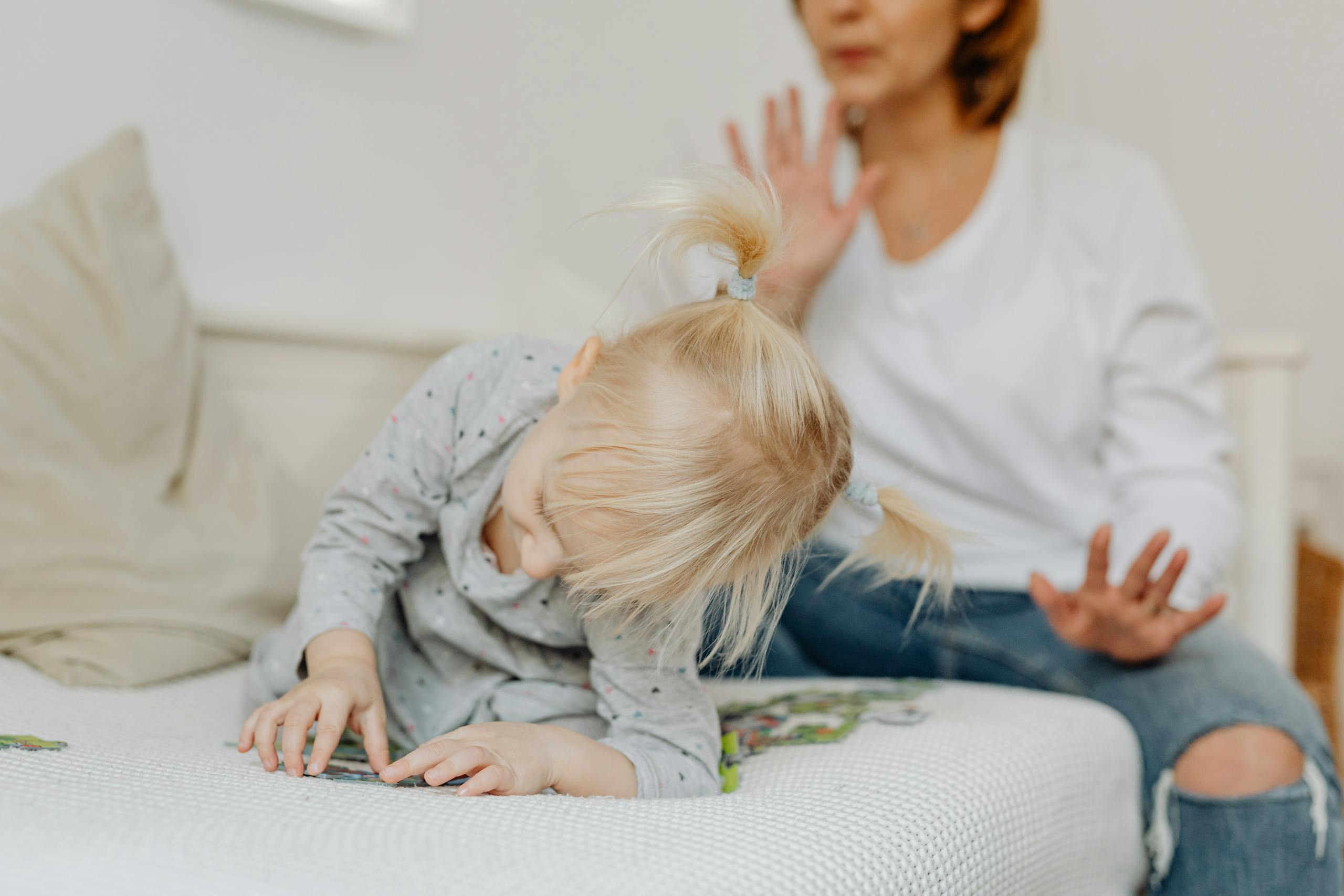 A young child and mother play on couch. Engaged in puzzles indoors.