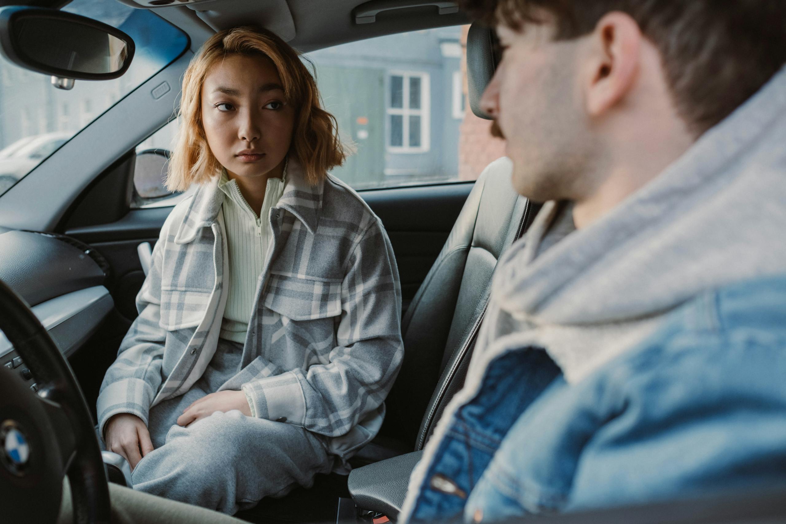 A young couple engaged in a serious conversation inside a parked car, capturing emotional tension.