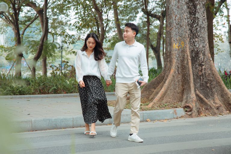 A young couple holding hands and strolling together in a serene park setting.