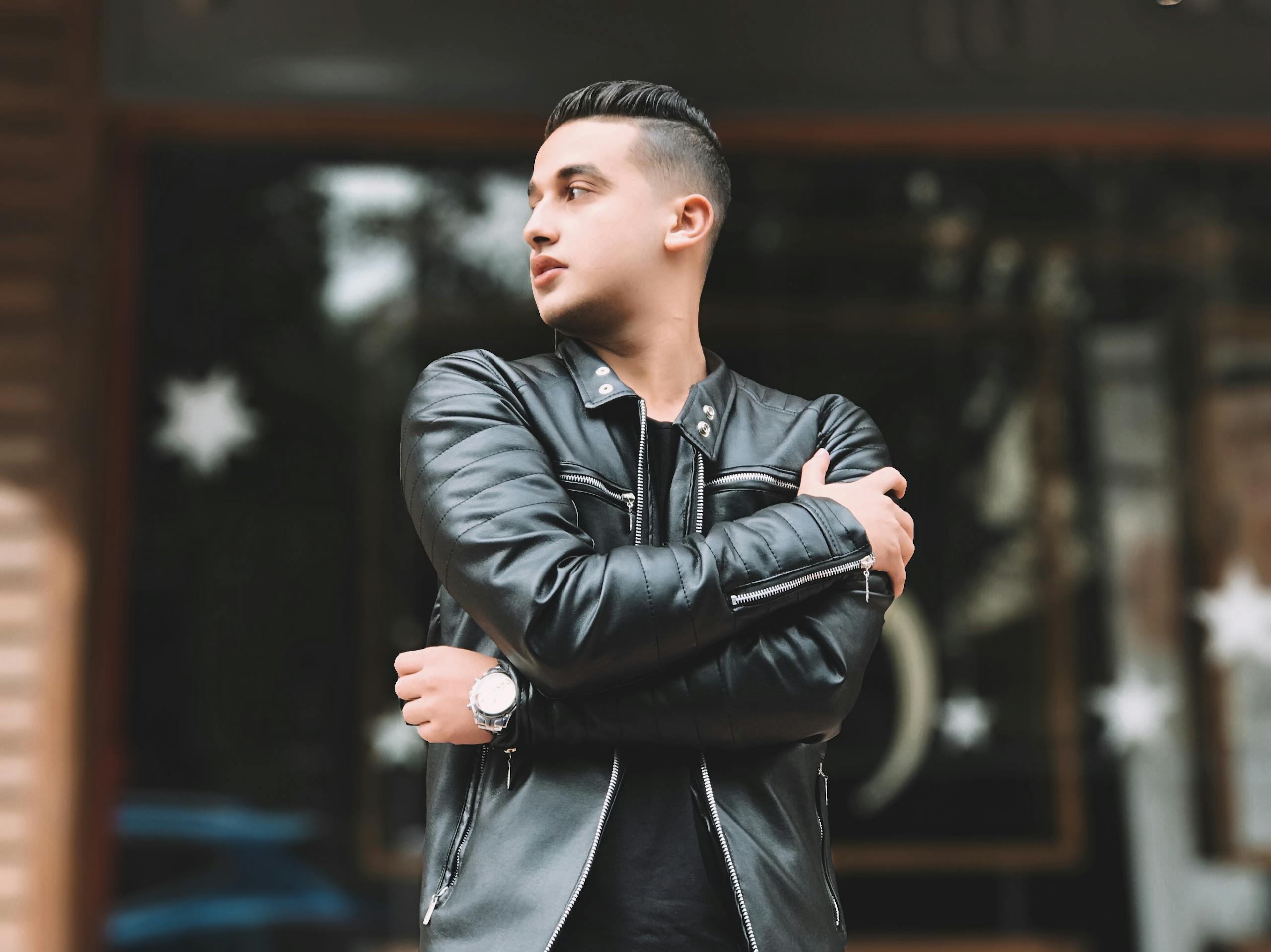 A young man in a leather jacket stands outdoors, embodying modern urban fashion.