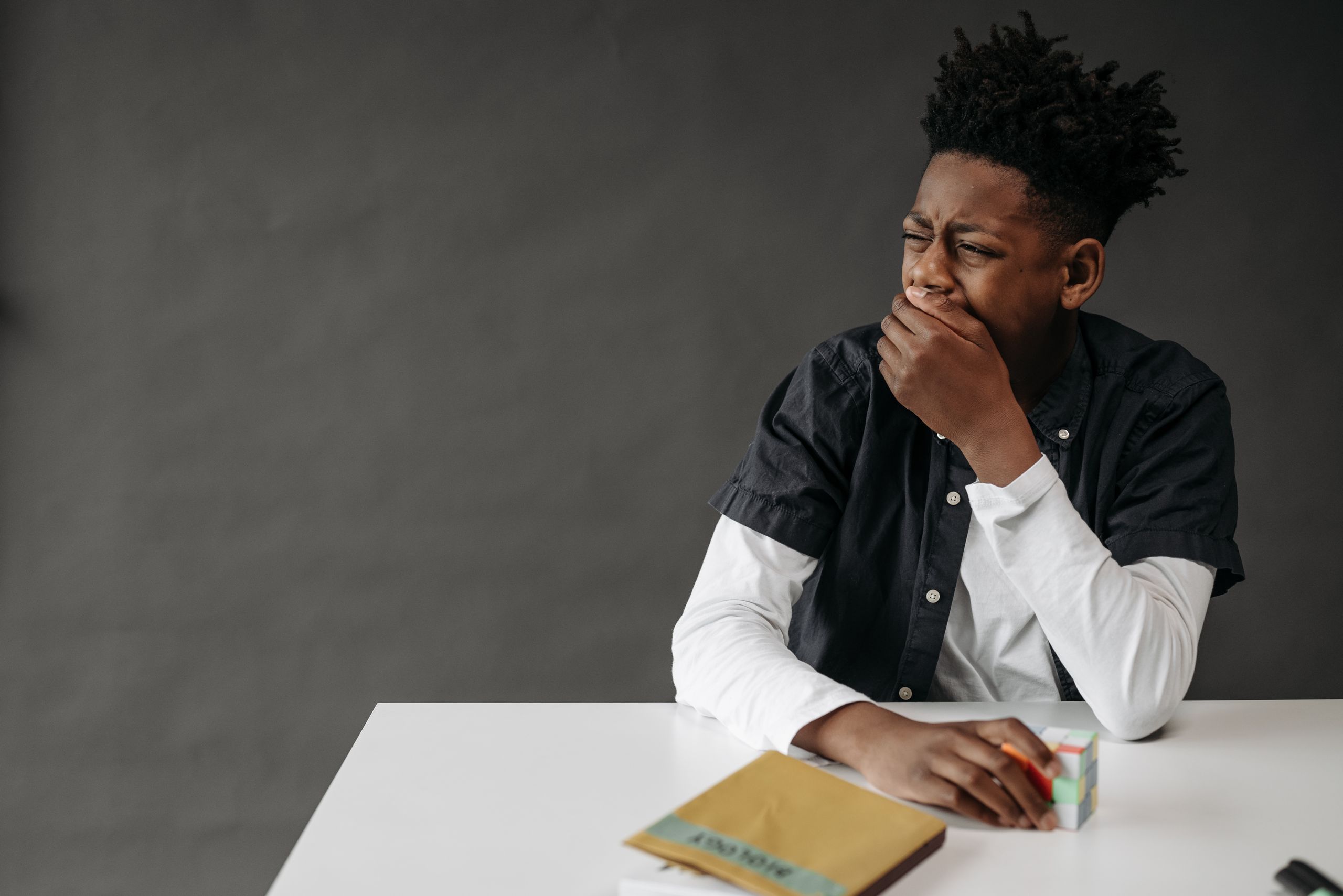 A young student with afro hair yawning at a school desk, appearing bored.