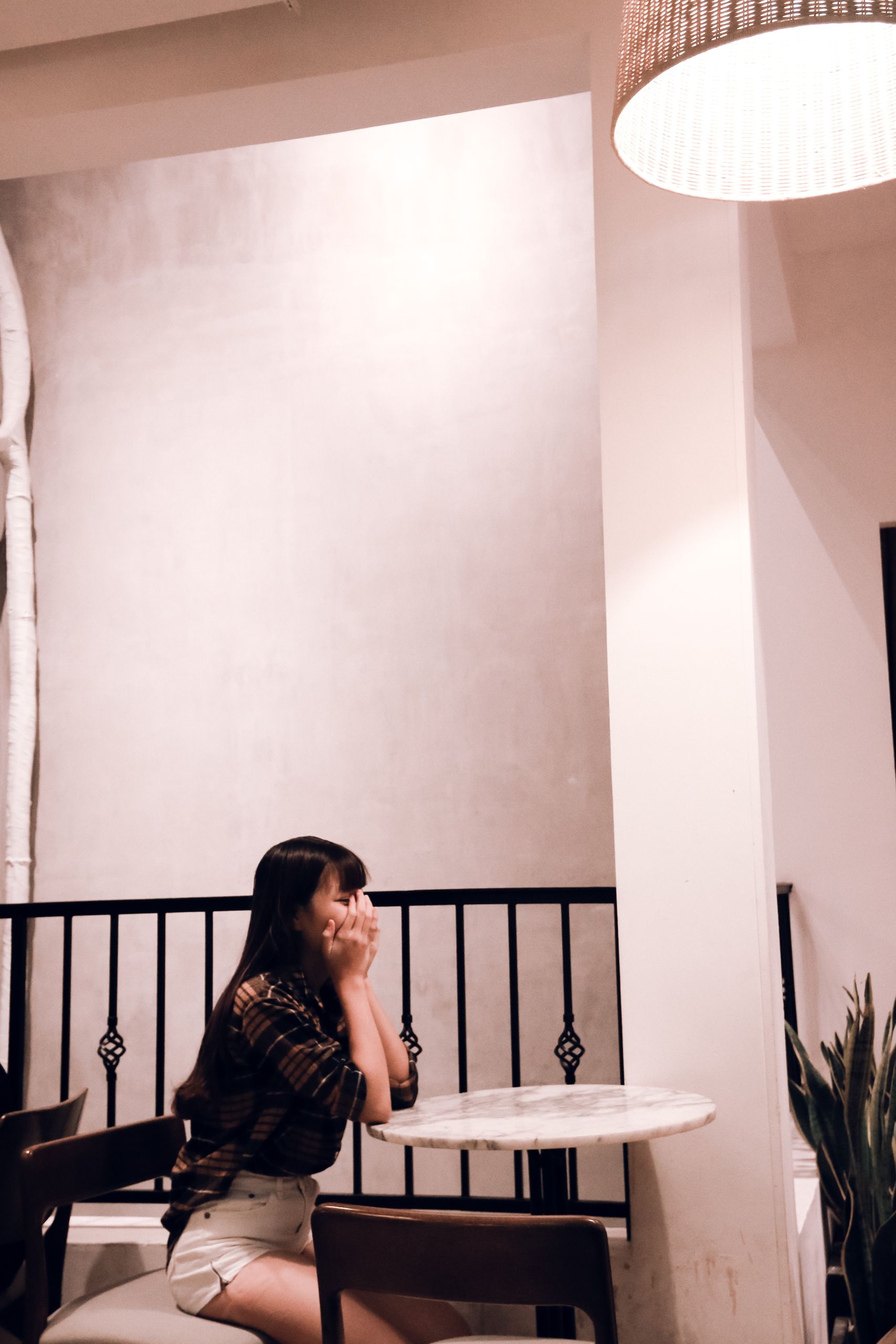 A young woman sits pensively in a stylish cafe. Warm lighting creates a cozy ambiance.