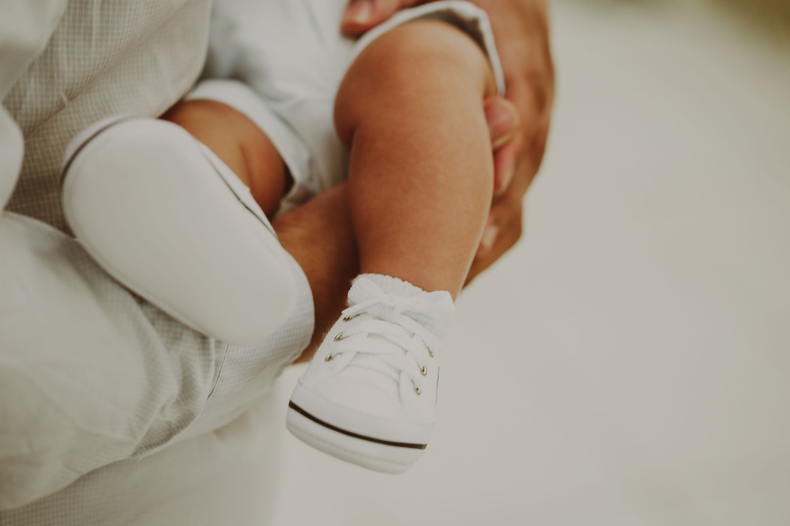 Adorable close-up of baby feet in white shoes being held tenderly.