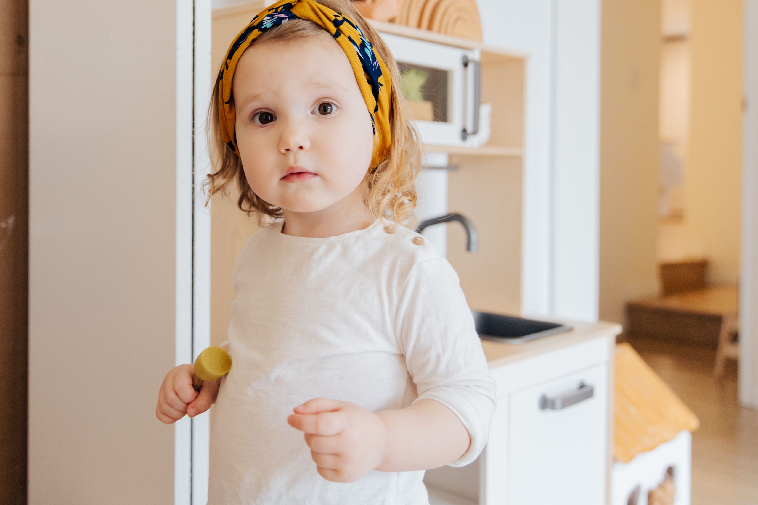Adorable toddler with yellow headband playing in a bright, cozy room.