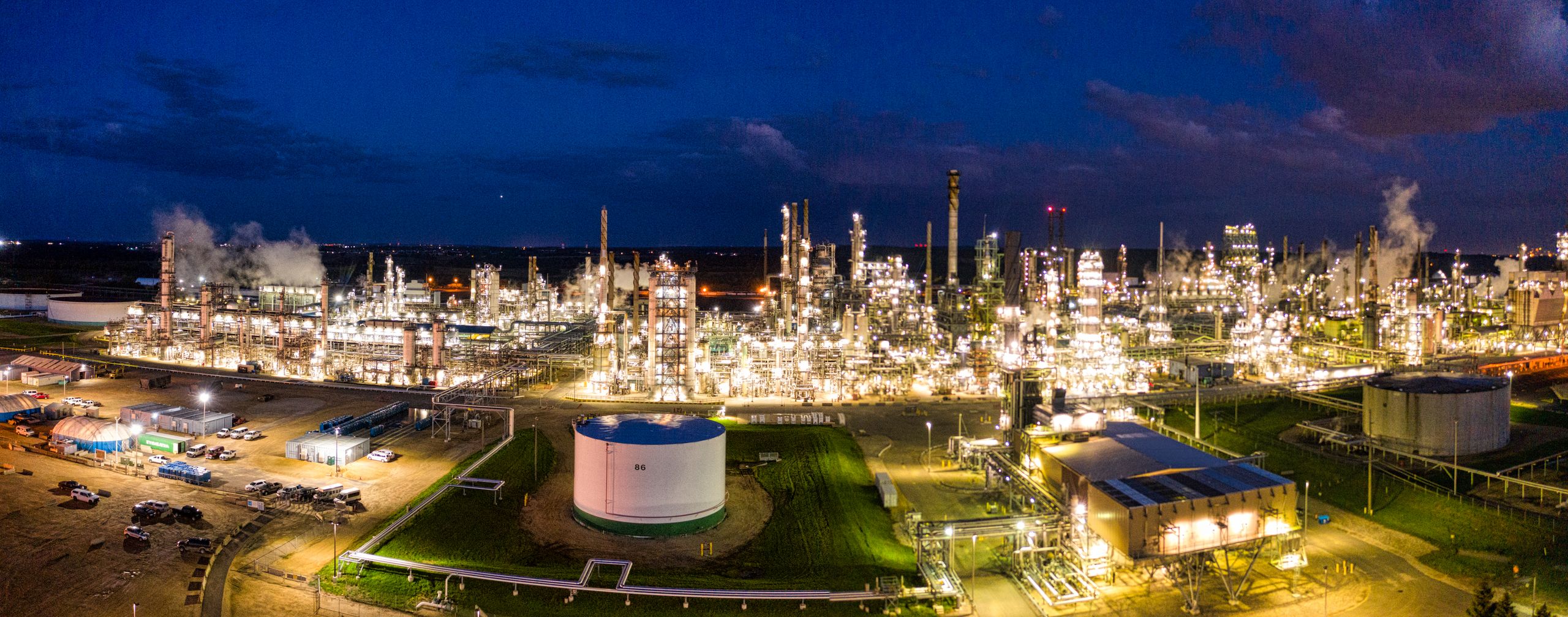 Aerial night view of a brightly lit industrial oil refinery with smoking chimneys in Rosemount, MN, USA.