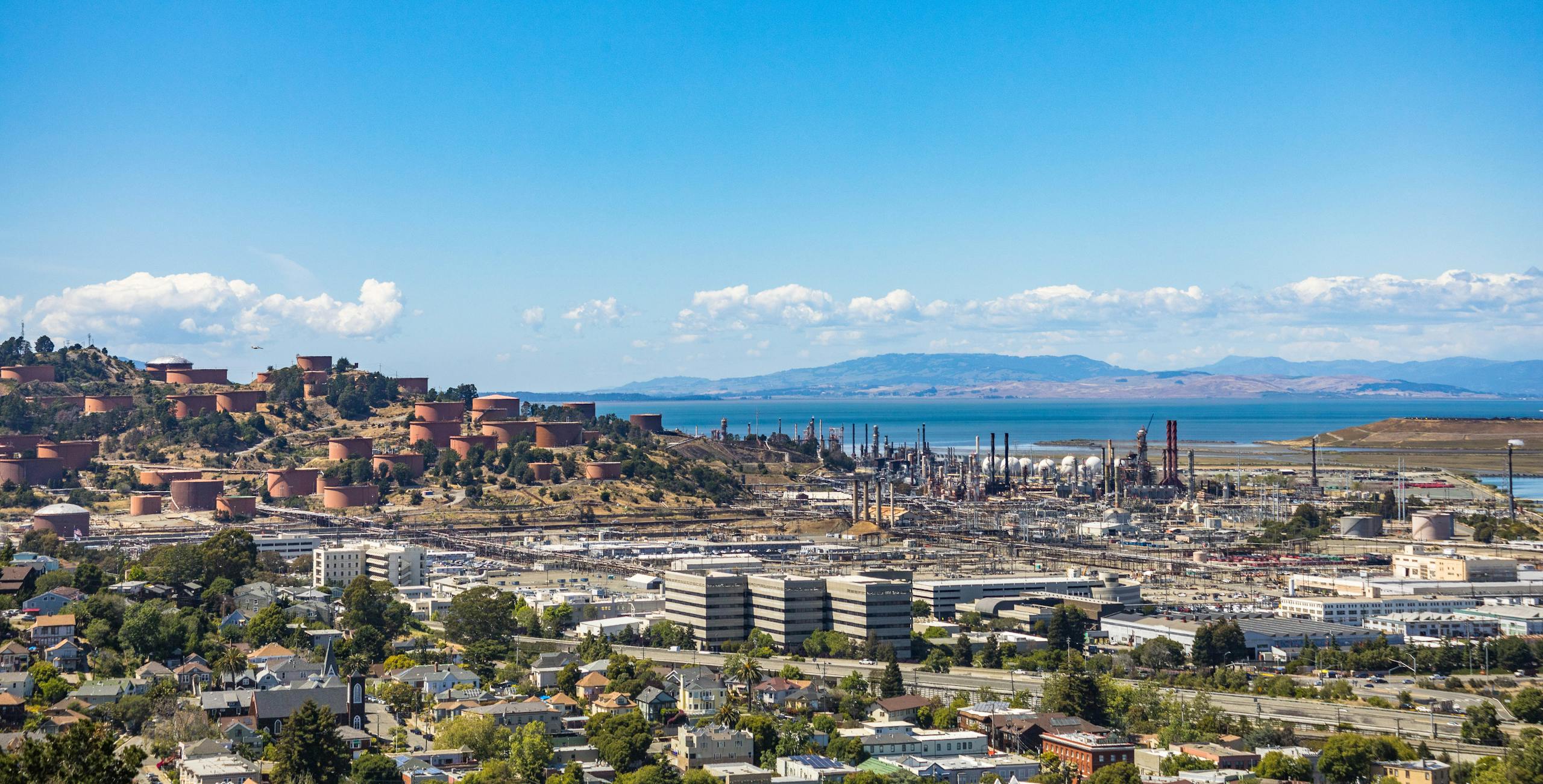 Aerial view of an urban area with an oil refinery by the sea and mountains.