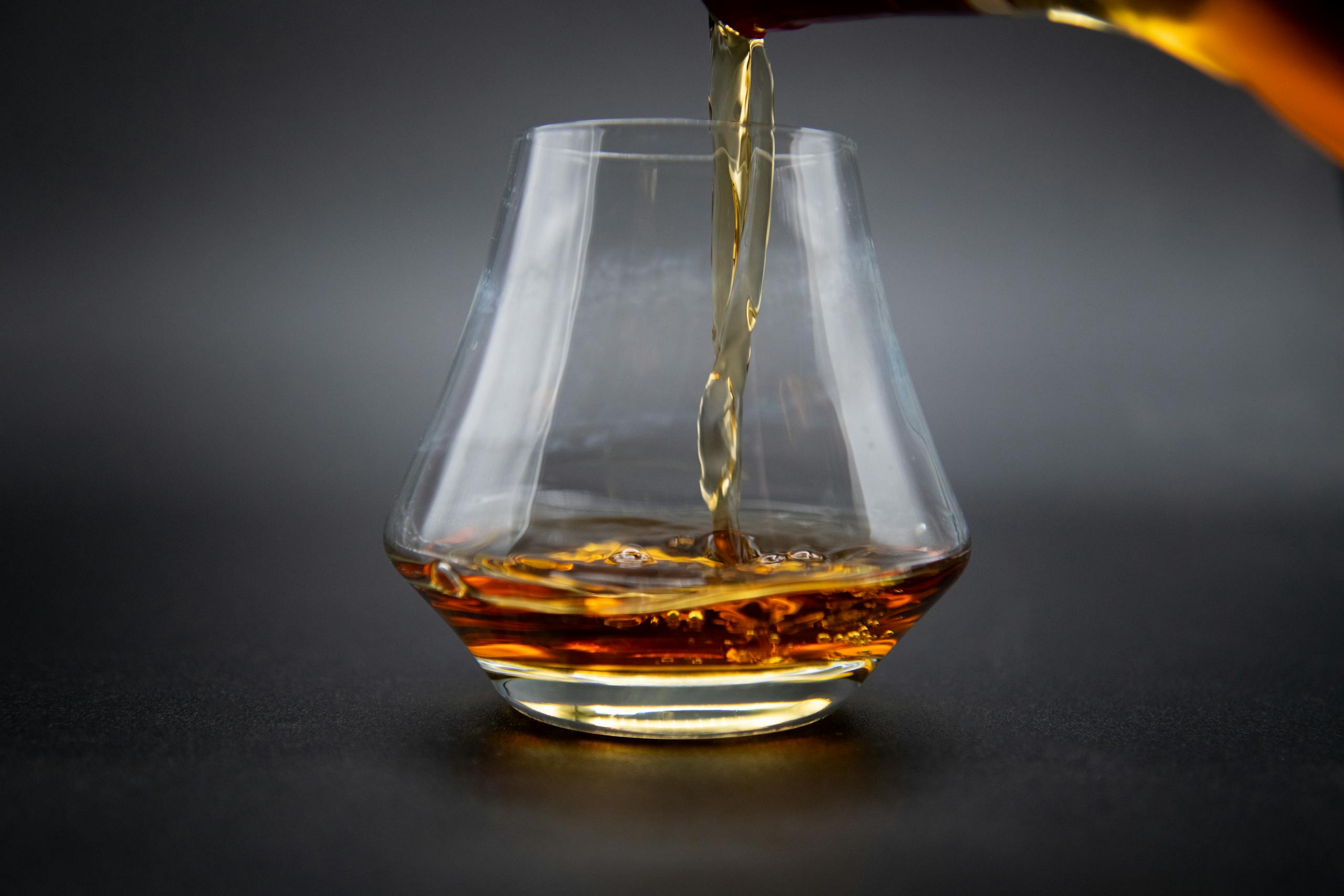 Aesthetic shot of whiskey being poured into a glass against a dark background.