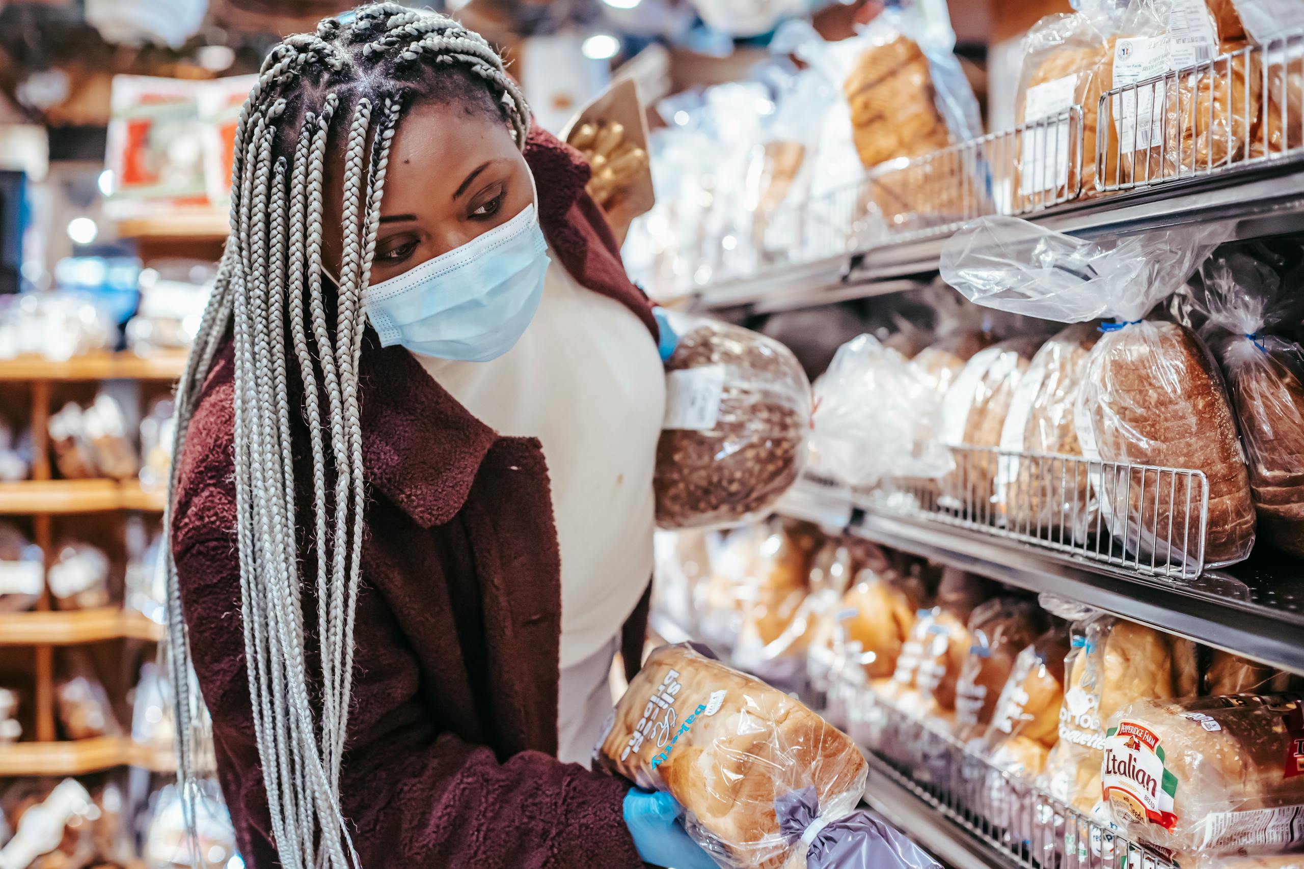 African American female customer in protective mask and gloves selecting bread in supermarket during coronavirus pandemic