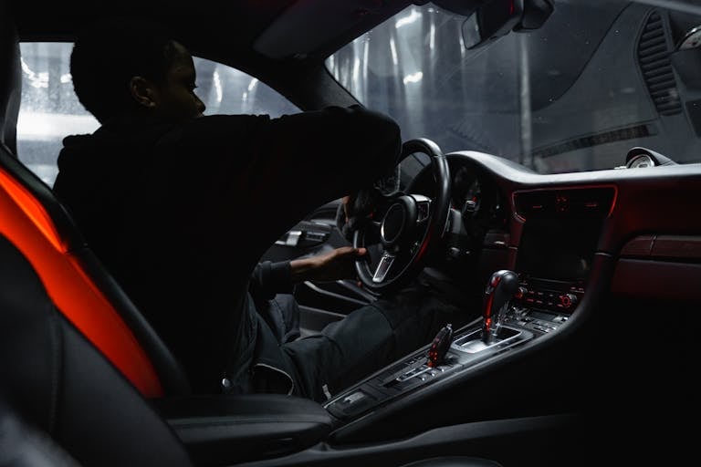 An African American man cleaning luxury car interior with focus on steering wheel and dashboard.