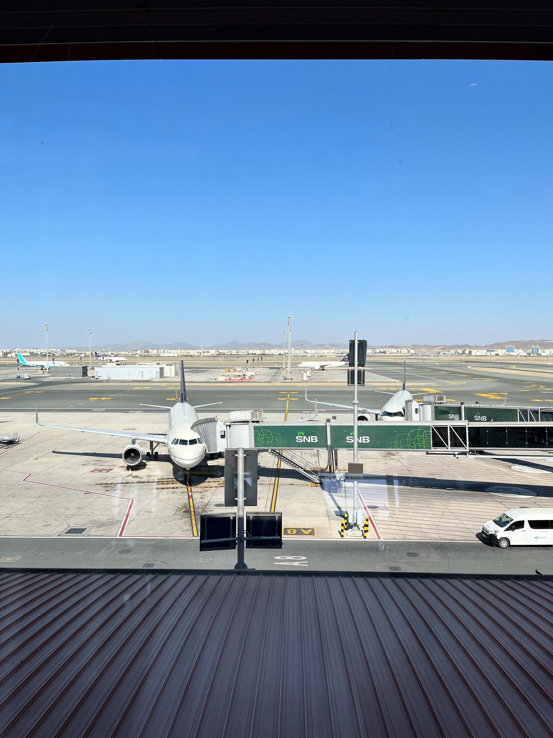 Airplane docked at terminal gate in Jeddah Airport, clear blue sky.