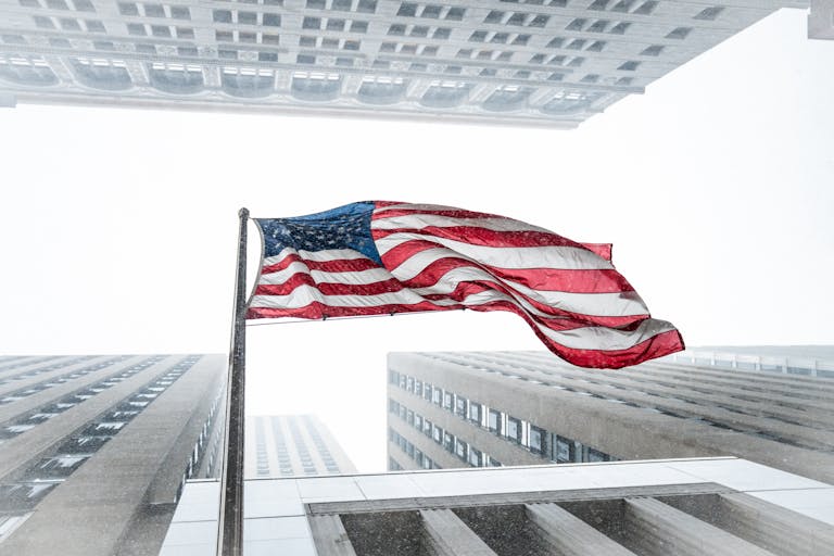 American flag waving amidst towering skyscrapers during a snowstorm in Chicago.