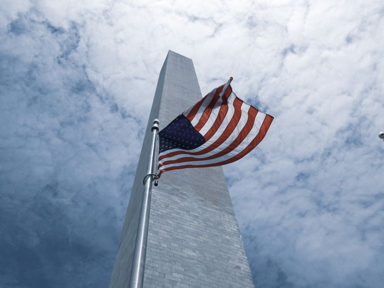 American flag waving in front of the Washington Monument under a cloudy sky in Washington, DC.