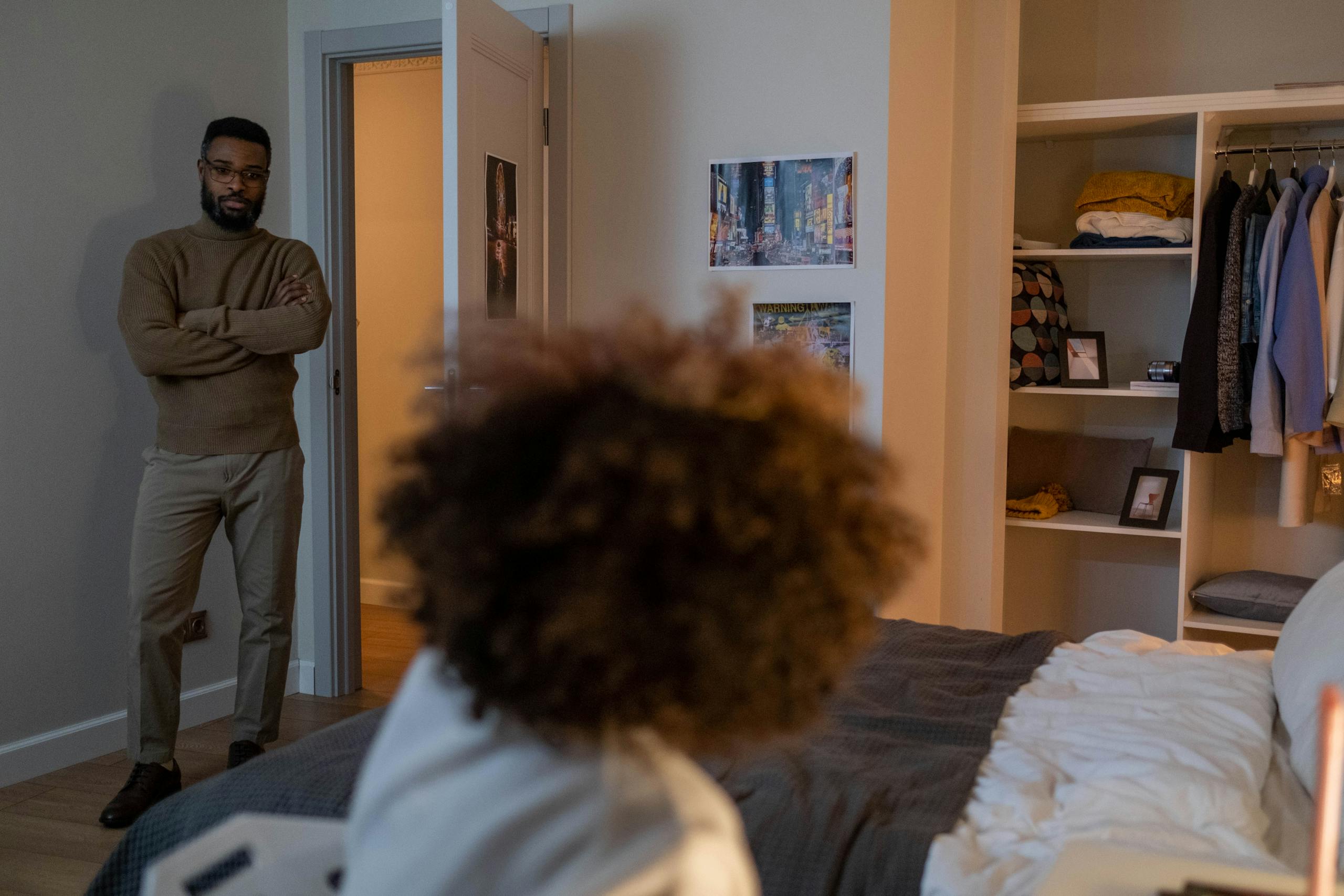 An adult standing in a bedroom, having a conversation with a seated child. Warm and inviting indoor scene.