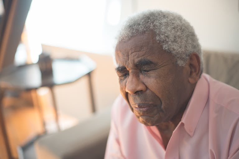 An elderly man with gray hair expresses deep emotion, sitting indoors in a moment of grief.