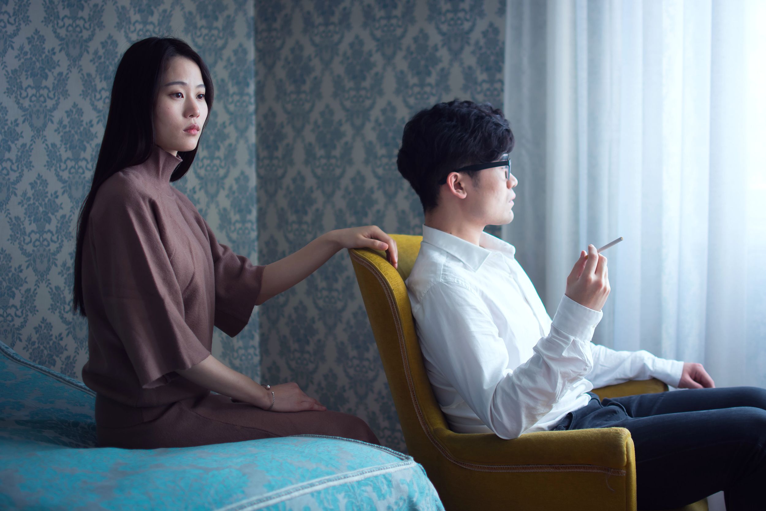An elegantly dressed couple sits in a vintage-styled room, creating a serene mood with soft lighting.