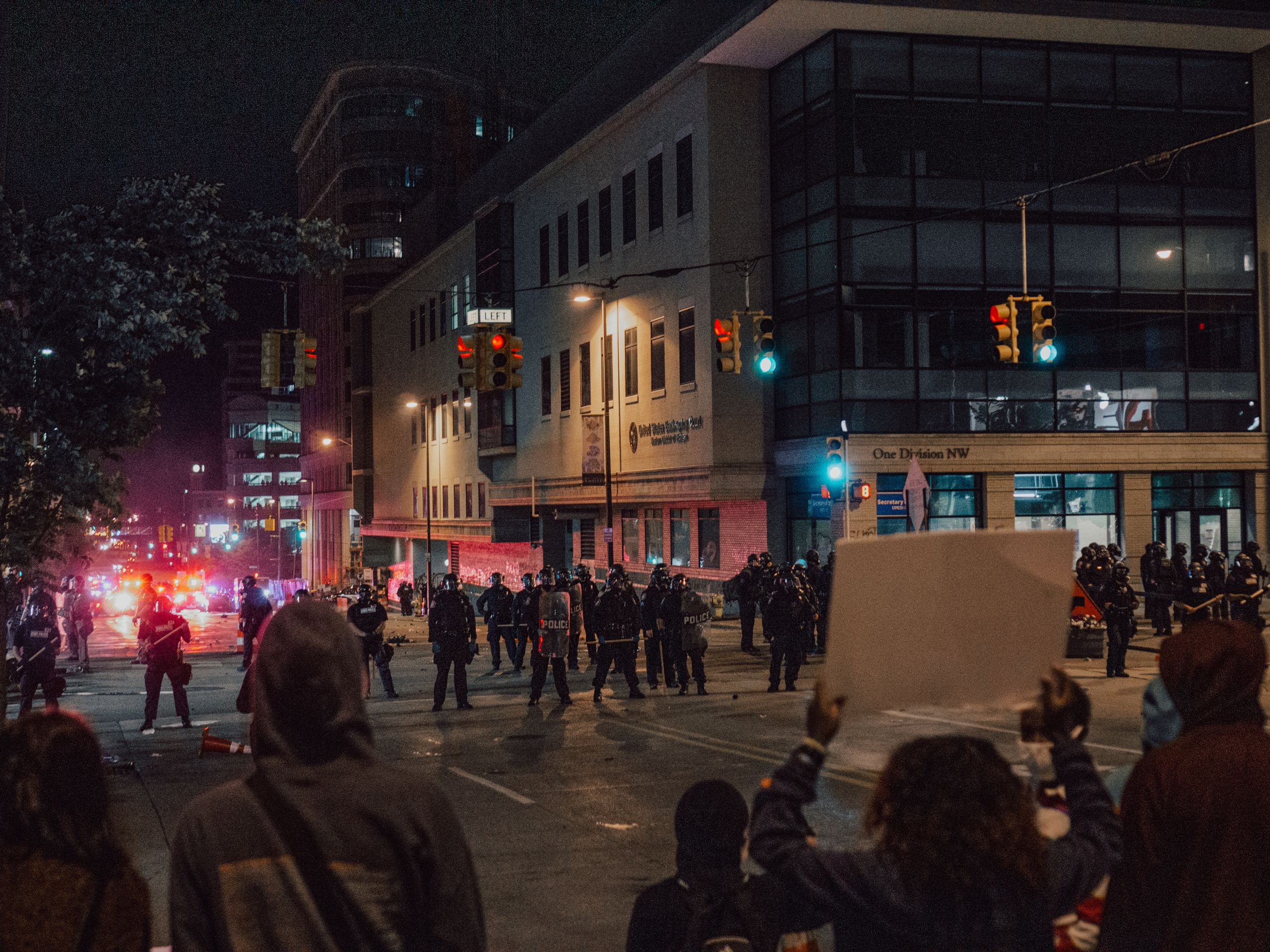 An urban protest at night with police and demonstrators on a city street.