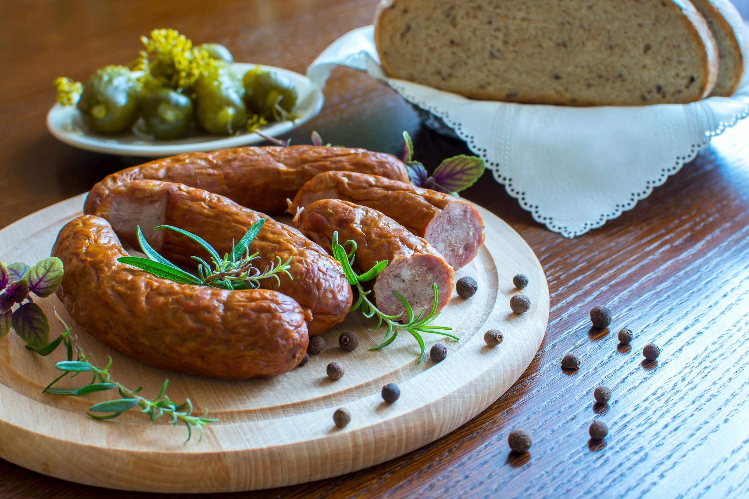 Appetizing smoked sausages on wooden platter with bread and pickles, perfect for a rustic meal.