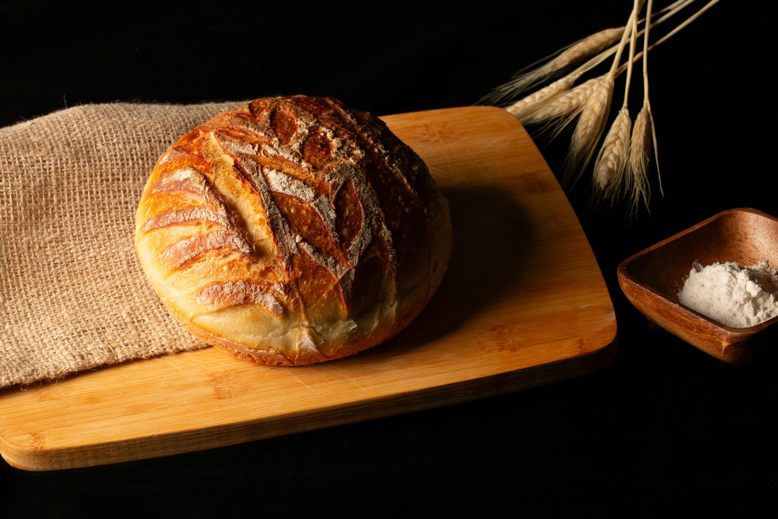 Artisan sourdough bread on a wooden board with wheat stalks and flour, capturing rustic bakery vibes.