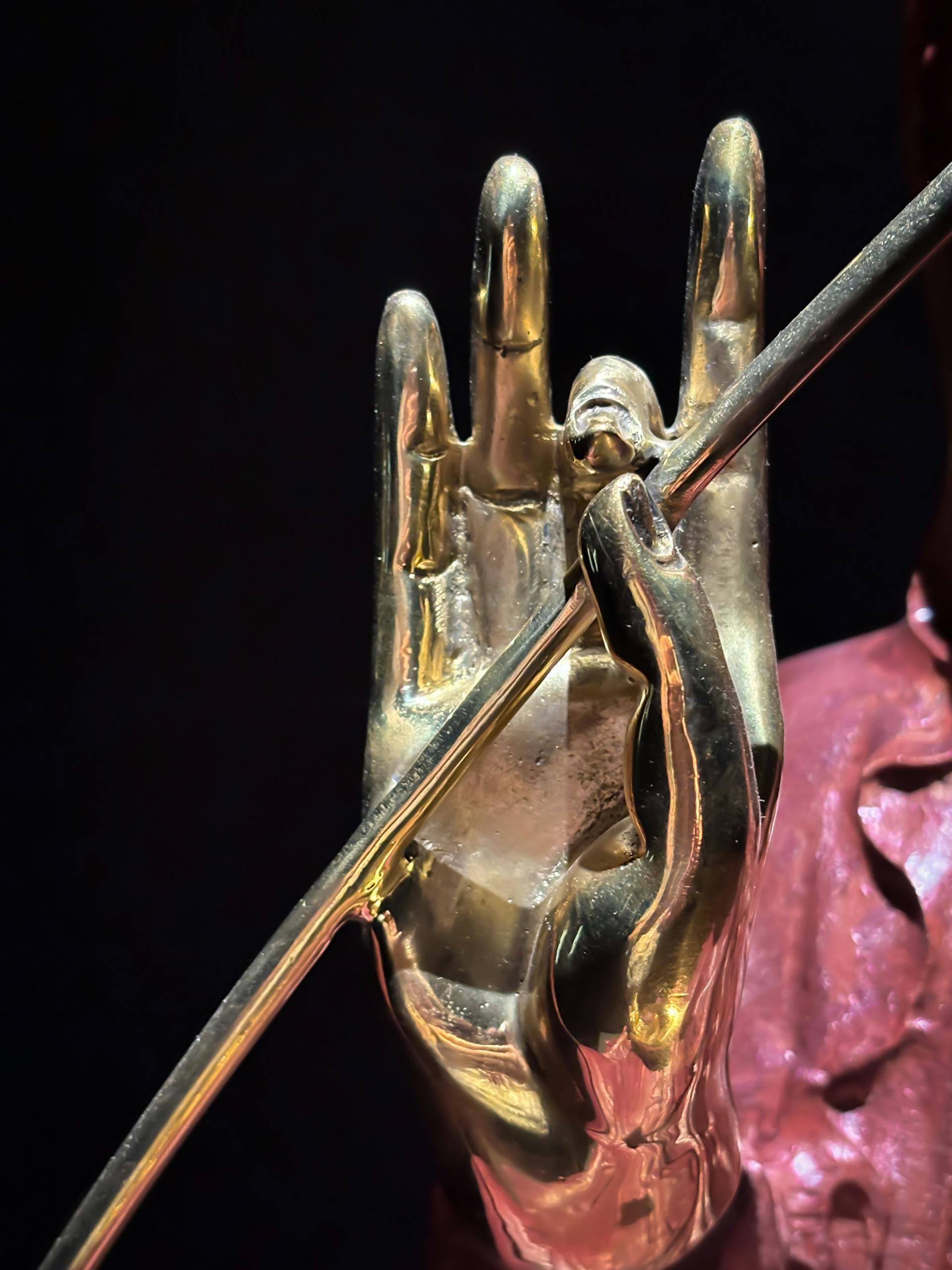 Artistic golden hand statue holding a rod, isolated on a dark background.