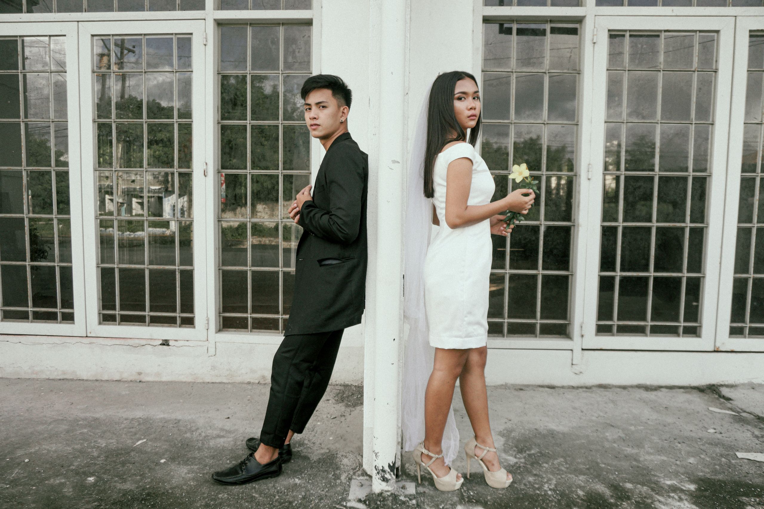Asian couple posing stylishly against modern glass windows for a photoshoot.