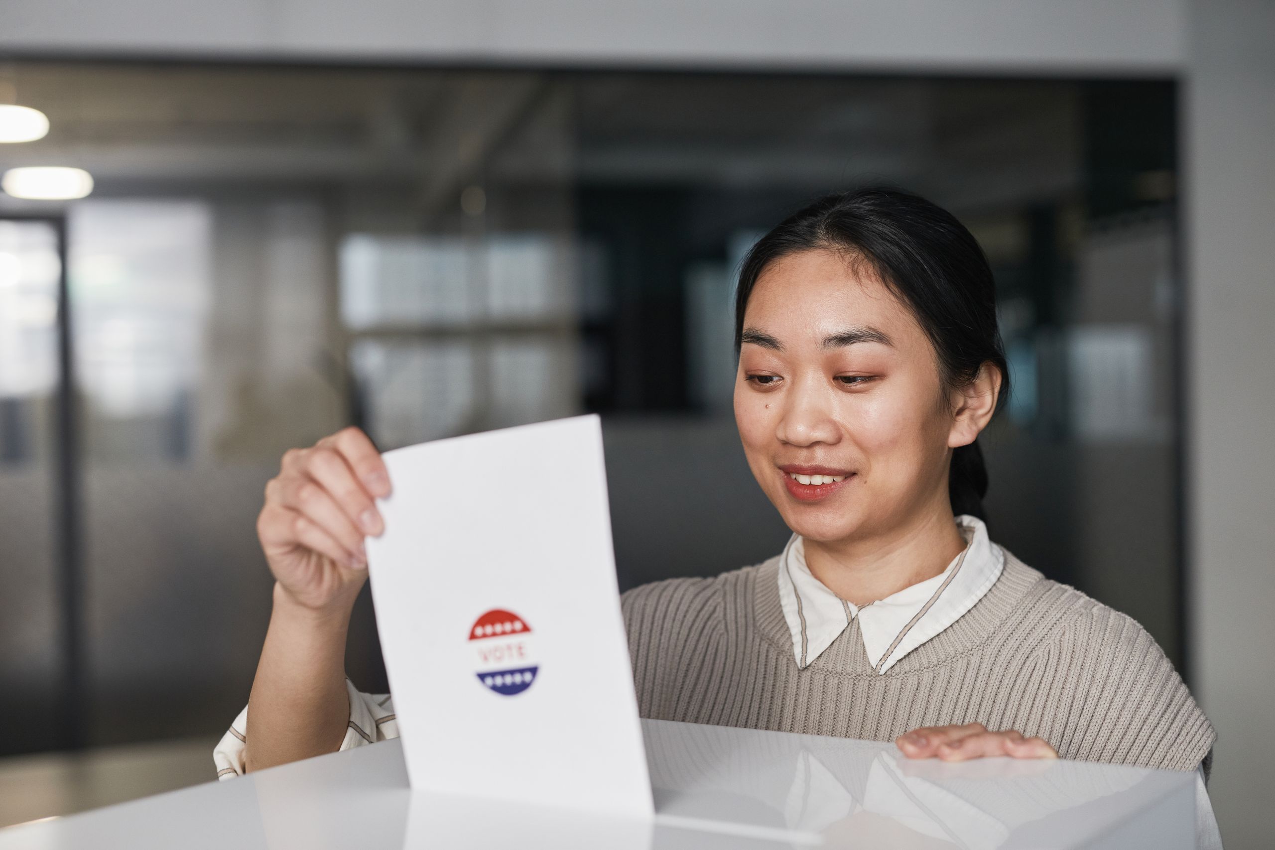 Asian woman placing a ballot paper into a box during an indoor voting session.