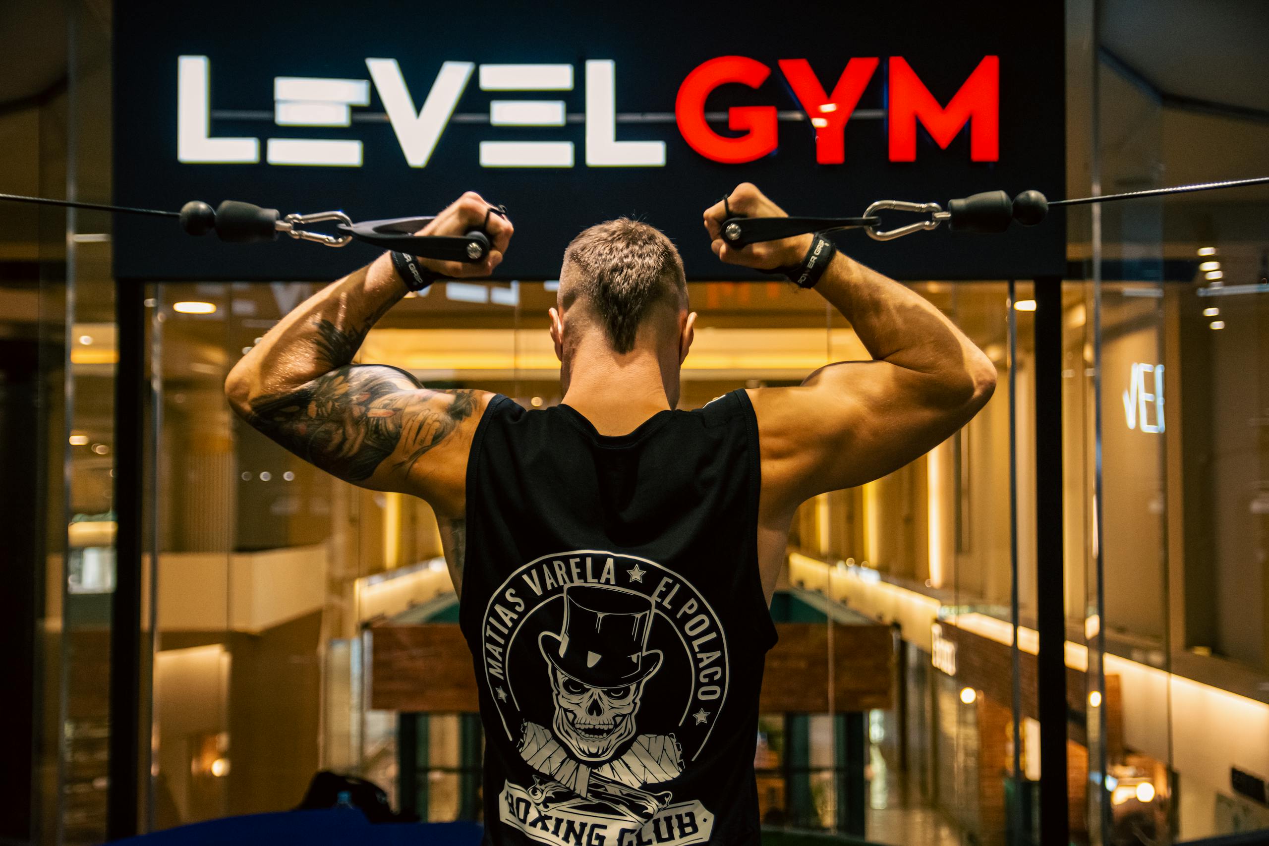 Back view of a muscular man working out in a modern gym, focusing on strength and fitness.