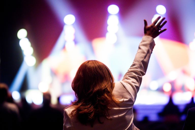 Back view of a woman raising her hand at a lively music concert, immersed in colorful lights.