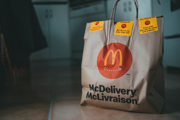 Beige package with bright yellow stickers and fast food on floor of apartment on blurred background