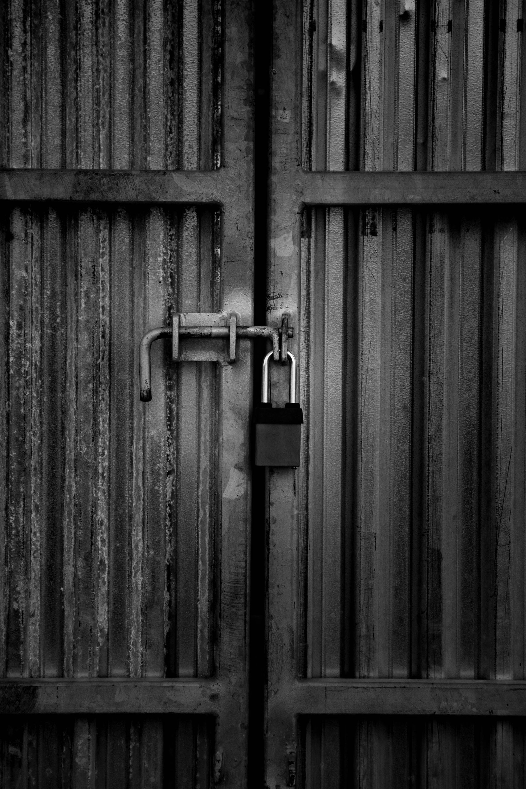 Black and white image of a padlock securing a corrugated steel door.