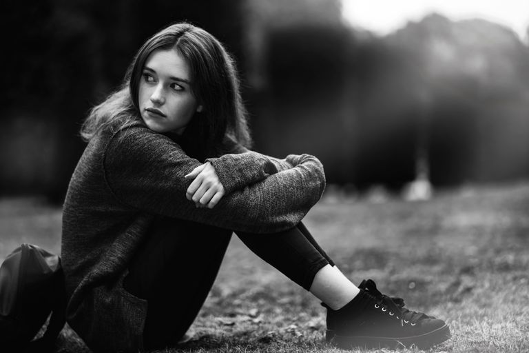 Black and white photo of a woman sitting outdoors, looking thoughtful and serene.
