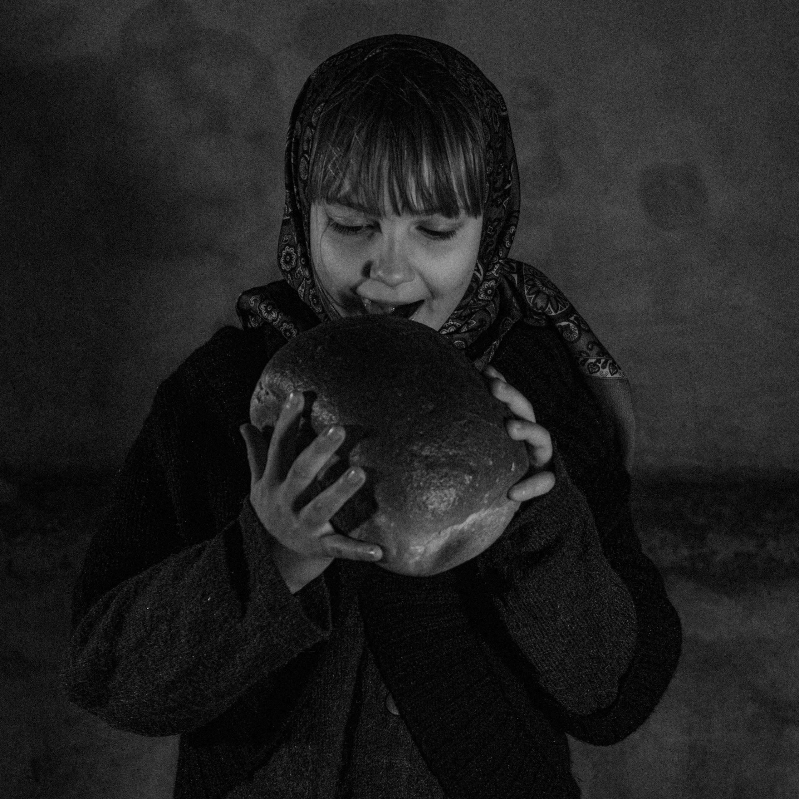 Black and white portrait of a girl eating bread, conveying hunger.