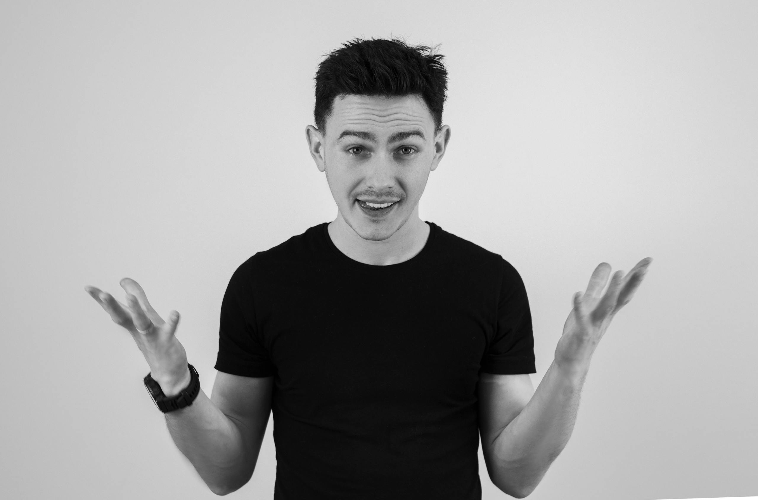 Black and white portrait of a man in a black t-shirt gesturing with open hands.