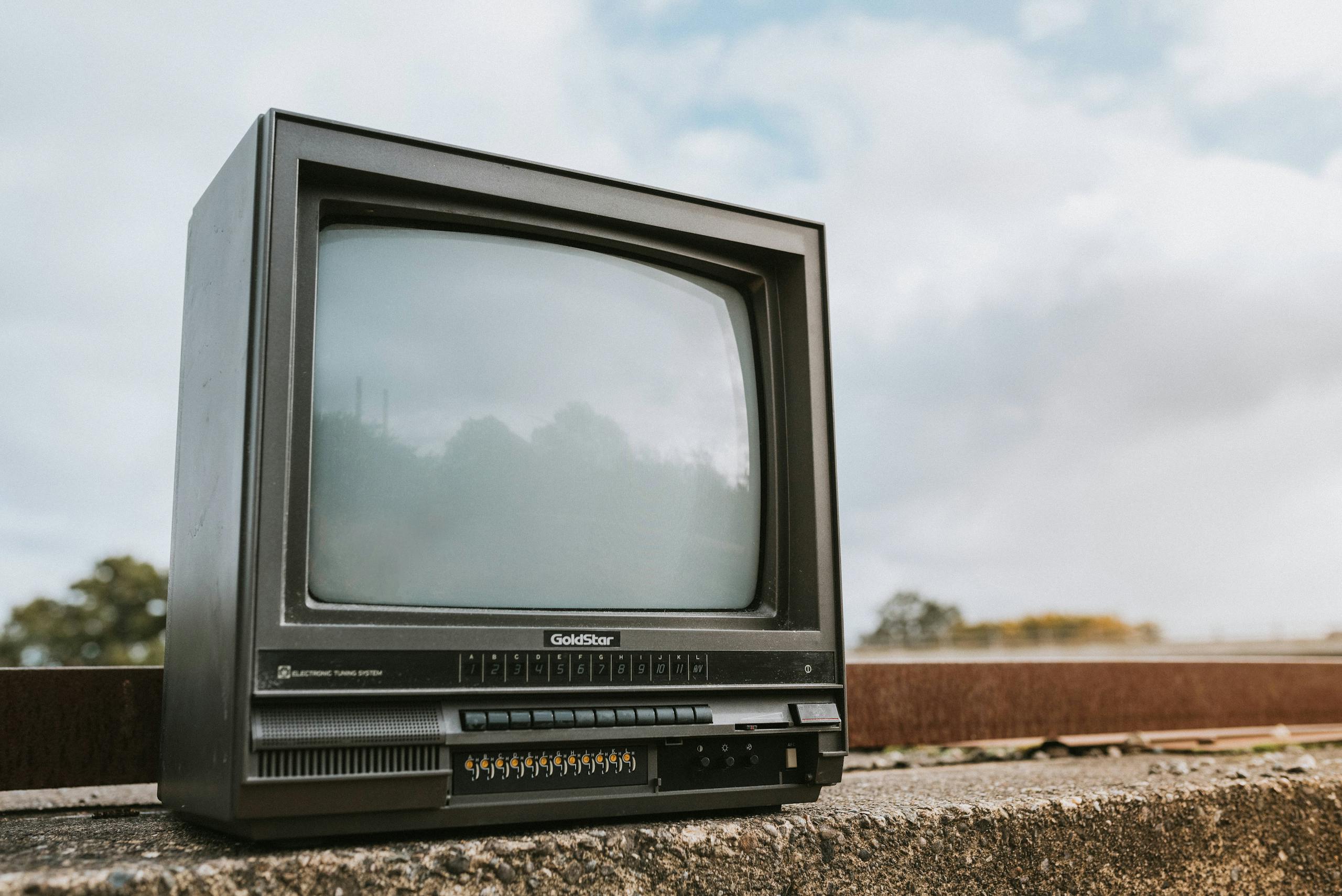 Black old fashioned obsolete television with reflection on screen placed on concrete railing against cloudy ski on street on blurred background
