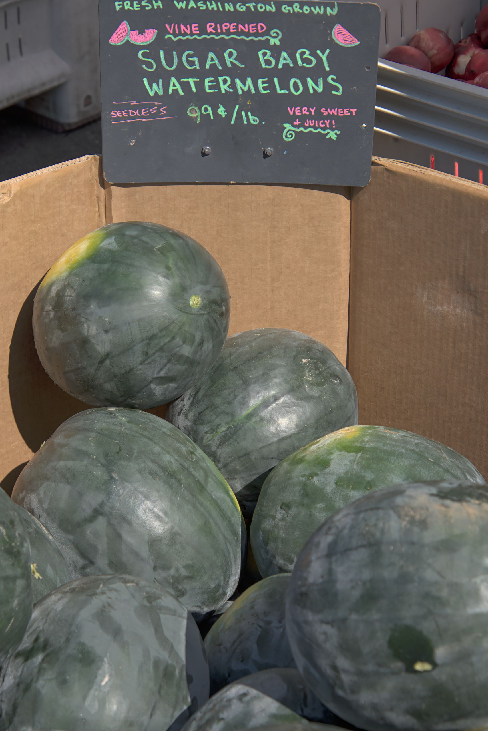 Box of vine-ripened Sugar Baby watermelons for sale at an outdoor market.