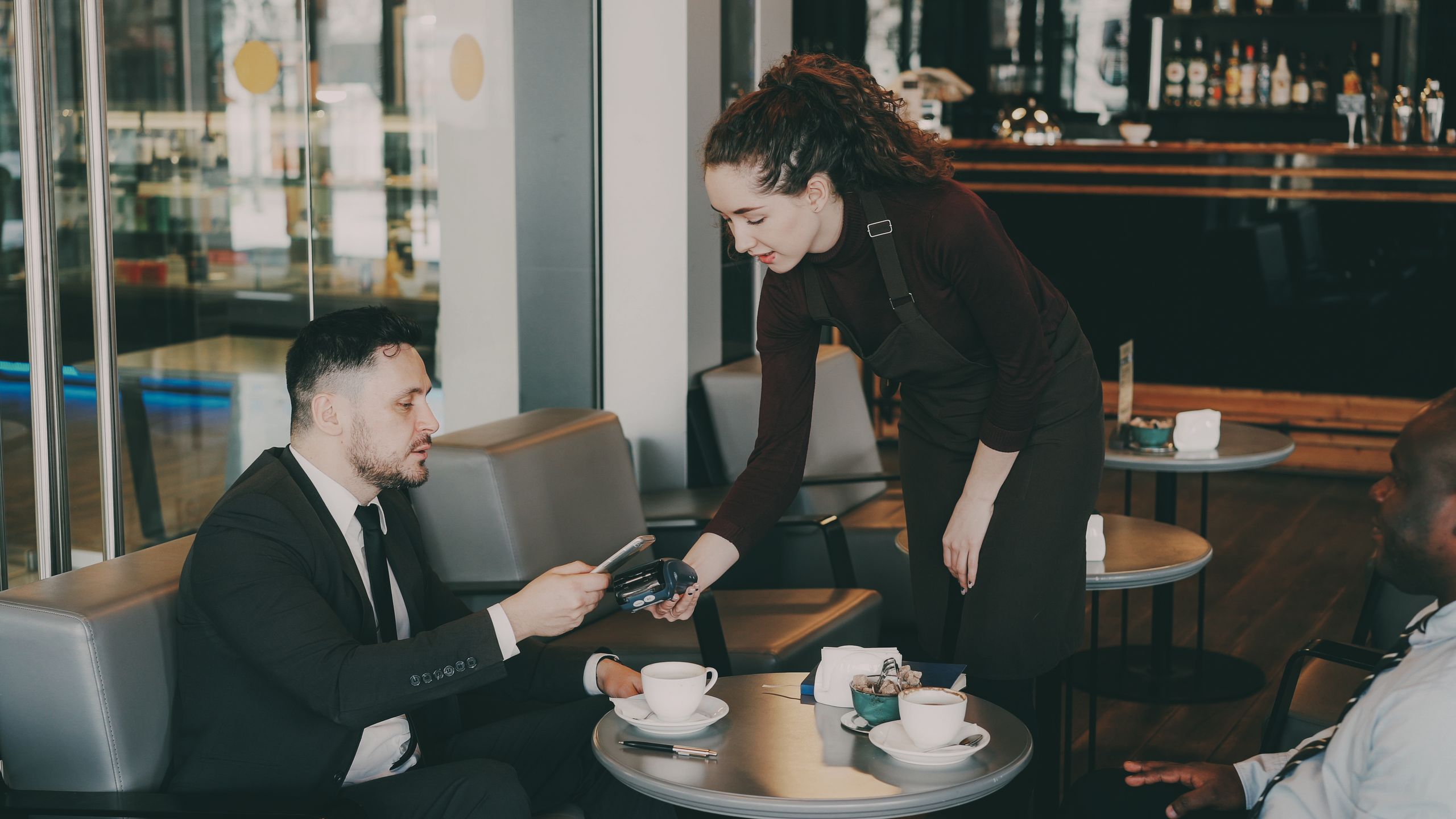 Business professionals in a café, paying with a card. Modern ambiance.