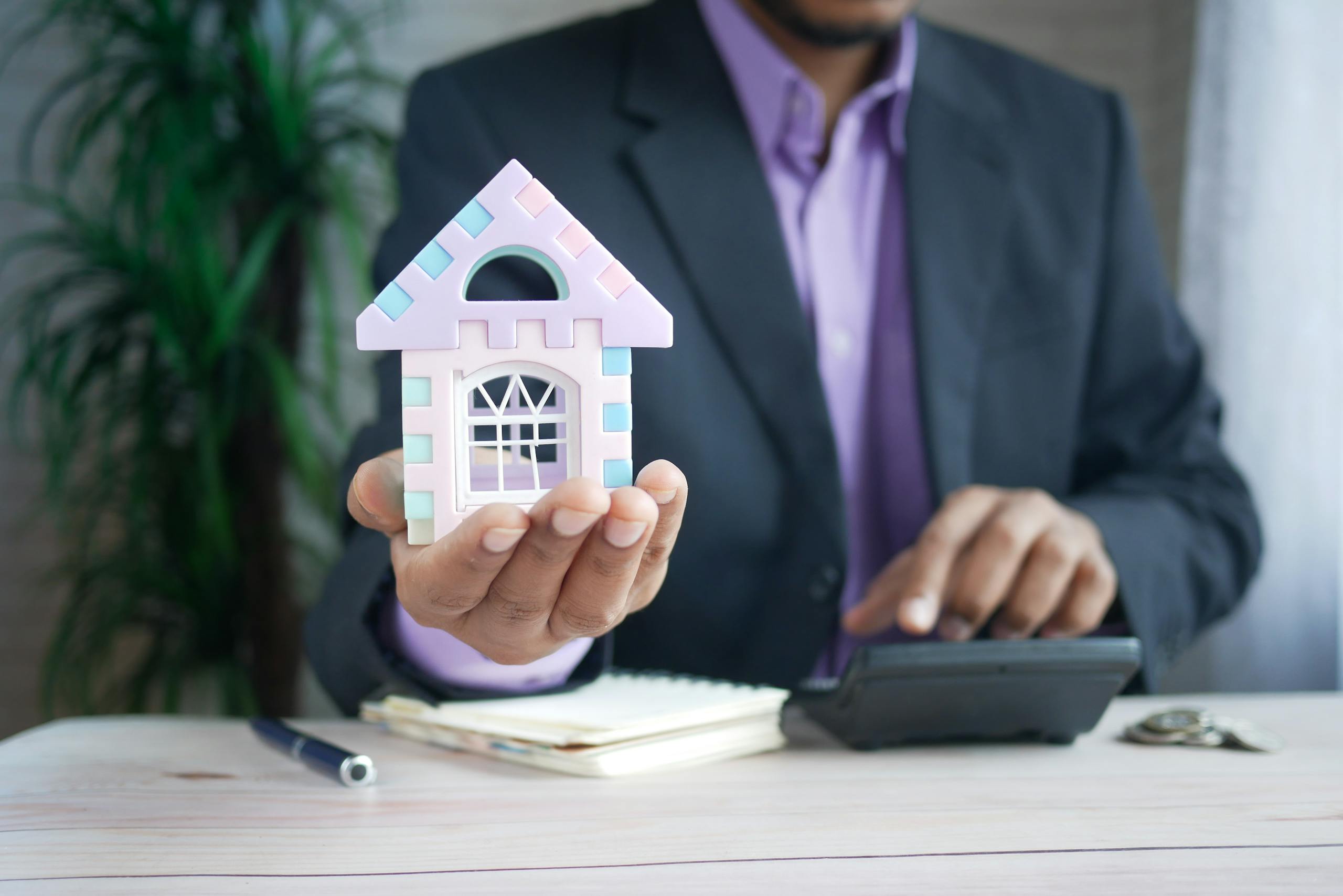 A businessman in a suit holds a model house, calculates real estate investments.