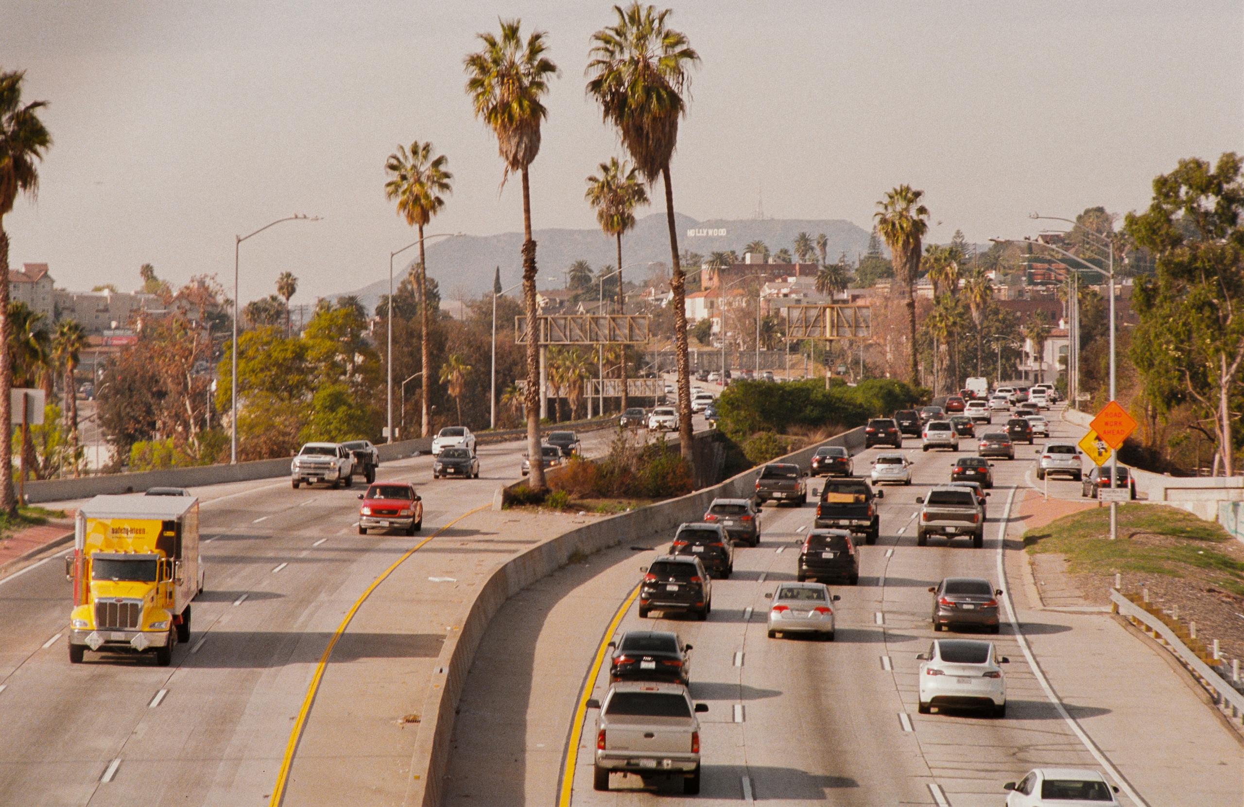 Busy highway traffic in Los Angeles with the iconic Hollywood sign visible in the background.