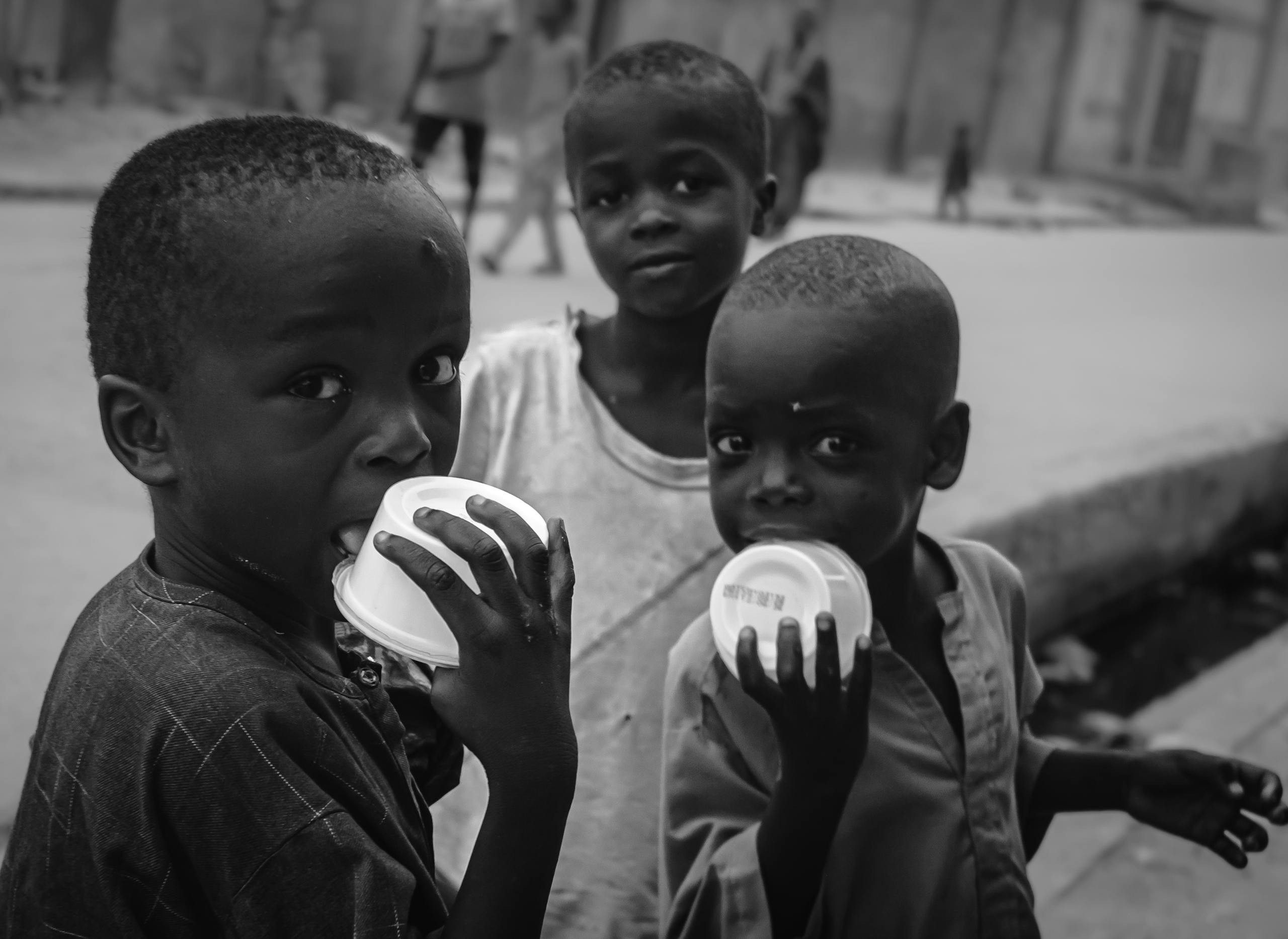 Candid street photo of children enjoying a treat, captured in black and white.