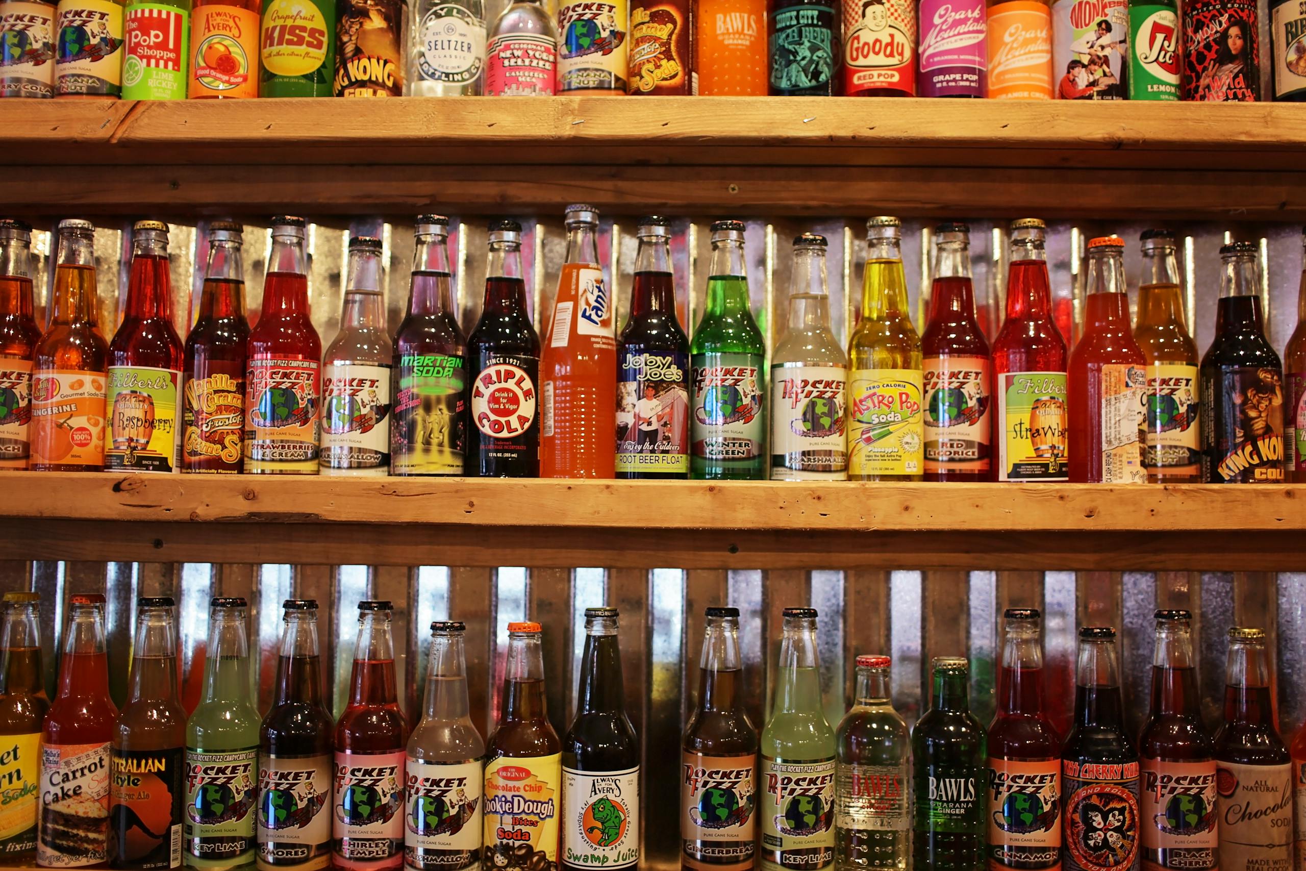 Carbonated drinks of different flavors in glass bottles on wooden shelf in store