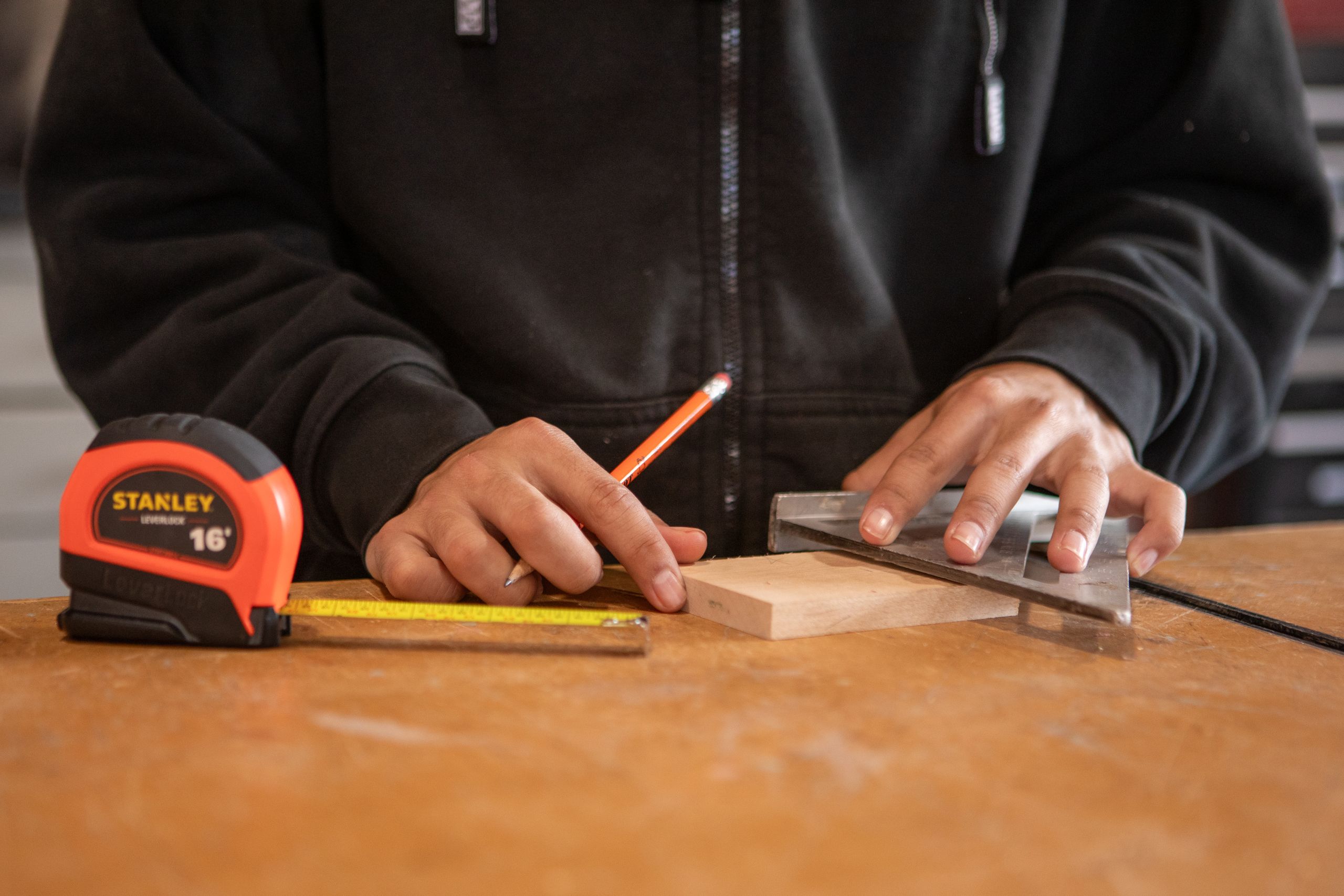 Carpenter using tape measure and speed square on wood block, ensuring accurate measurements.