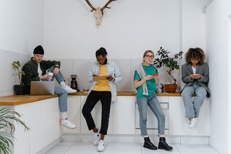 Casual and diverse colleagues using gadgets in a modern office kitchen area.